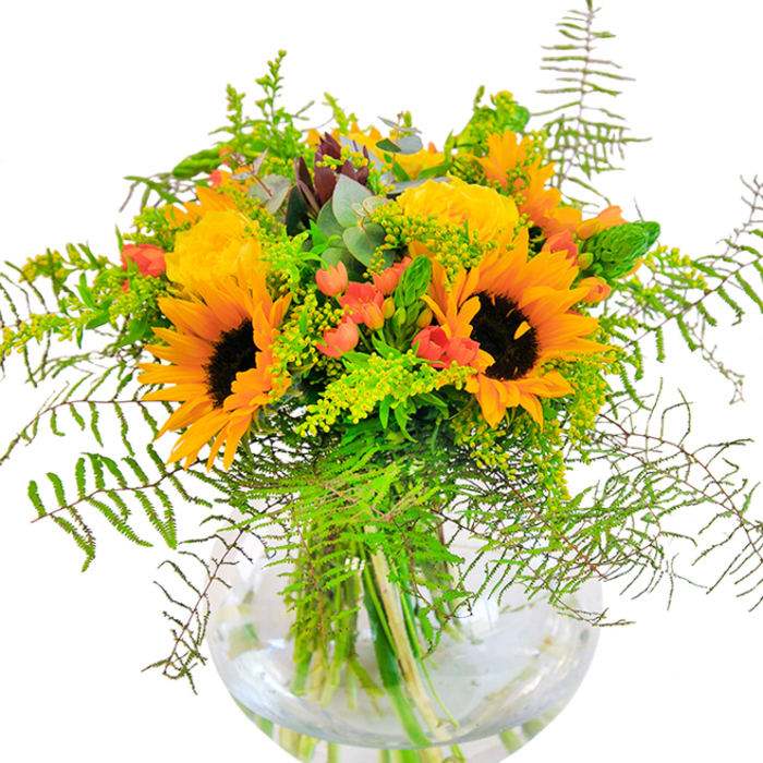 From the first glance, this glowing bouquet suggests a sun-drenched day in Epping, alive with the exuberance of large sunflowers and soft, amber roses. The sunflowers reach outward with generous petals and dark, striking centres, their golden hues harmonising with the tightly layered, spiralling roses for an effect both jubilant and refined. Deep, glossy red Hypericum berries gleam among the lush greenery-crisp ferns, airy filler, and the slender spikes reminiscent of the foliage found along the border of Epping's open spaces. The interplay of textures is captivating: the downy petals of the sunflowers, the silk-wrapped roses, the crisp freshness of the green, and the velvety cascade of feathery ferns. Eucalyptus fronds introduce a cool green note and a subtle, clean perfume that feels like a breeze through Epping Forest. The arrangement is anchored in a clear round vase, allowing the marbled stems and sparkling water to echo the clarity of a summer morning. Lively, cheerful, and thoughtfully composed by expert Epping florists, this bouquet brings a celebratory spirit-perfect for milestones, heartfelt thank-yous, or brightening a table along Lindsey Street. Every element reflects the creativity and pride of local floral design.