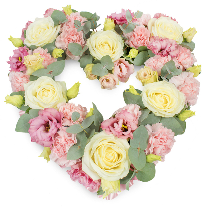 This image shows a beautifully crafted heart-shaped wreath, overflowing with pastel flowers and soft greenery, photographed against a bright white background that accentuates its colours and details. The heart is dense and complete, every part filled with blooms so that it appears plush and luxurious, like a floral embrace. Creamy yellow and ivory roses are dotted evenly across the design, their generous, tightly layered petals spiralling outwards to form classic, cup-shaped blossoms that serve as the main visual anchors. Between these roses, clusters of pale pink carnations form a gentle, textured weave, their frilled edges and rounded heads creating a sense of movement and cushioning. Among the paler tones, deeper magenta-pink lisianthus flowers emerge, their slightly ruffled, open blooms adding a graceful curve and a richer note of colour that lends quiet sophistication, much like the character of Epping's historic High Street. Silvery-green eucalyptus leaves thread through the arrangement, their round, satin-matte foliage offering a cool, calming contrast to the warmer petals while also helping to outline the heart's smooth edges. Here and there, tiny yellow-green buds can be spotted peeking out from the floral mass, hinting at freshness and the idea of life continuing on. The overall impression is one of tenderness, compassion, and enduring affection, making this heart wreath a thoughtful choice for funeral flowers, church services, or crematorium tributes in and around Epping. It feels like a gentle, wordless message, crafted by skilled local florists to honour a special relationship and surround a farewell with quiet beauty.