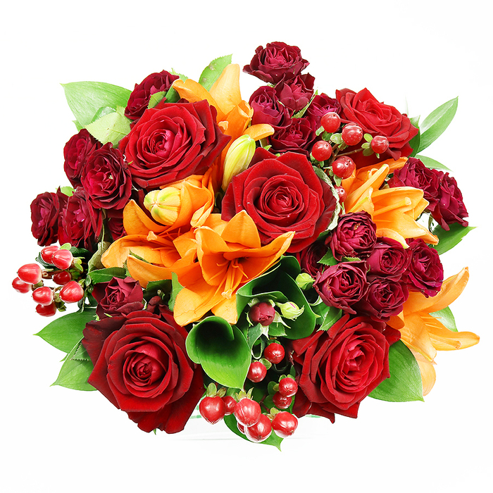 Captured from above with even, flattering light, this luxurious bouquet sits crisply against a white background, its perfectly rounded silhouette packed with blooms that read like a warm, sophisticated palette. At the heart are several large, fully bloomed deep red roses whose velvety petals curve outward in graceful spirals; their tactile richness provides a central anchor of classic romance. Bright orange Asiatic lilies thread through the composition, some fully open to display trumpet-shaped petals and prominent stamens, others held in tightened buds that promise continued bloom; the lilies' energetic colour introduces a lively contrast to the deeper reds. Interspersed throughout are small, dense spray roses in deep burgundy tones-each cluster contributing plush texture and layered colour depth-and glossy, red Hypericum berries that add playful, reflective dots across the arrangement. Fresh green foliage, likely ruscus or salal with broad, glossy leaves, breathes between the flowers, offering a cooling counterpoint and sculptural lines that accentuate the bouquet's fullness. The soft lighting highlights petal edges and the subtle sheen of berries while avoiding harsh shadows, making each element readable and richly detailed. This piece feels celebratory and refined, perfect for marking anniversaries, special dinners, or gifting to someone whose presence you wish to honour. It's the kind of arrangement our regular customers from St John's Road and the nearby church congregations in Epping often request-balanced, fragrant, and undeniably generous in spirit.