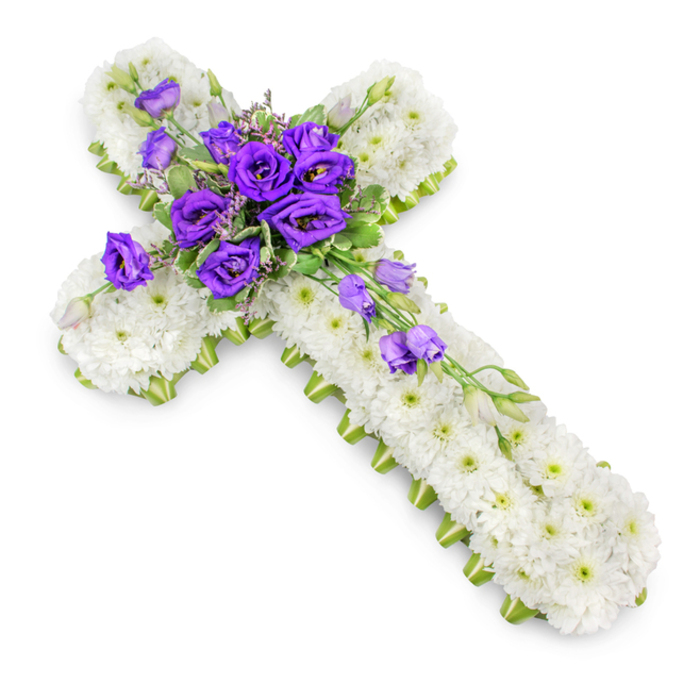 This image captures a traditional floral cross tribute, meticulously crafted and presented on a spotless white background that allows the design to stand out in full clarity. The cross itself is completely covered in white spray chrysanthemums, each flower carefully placed so that their petals overlap slightly, creating a continuous, plush texture. The blooms are uniform in size and tone, their white petals giving off a cool, pristine impression, softly contrasted by the delicate green centres peeking through. Surrounding the entire outline of the cross is a fine edge of lime-green ribbon, which hugs the contours of the arms and stem with precision. This ribbon acts as a gentle frame, adding definition and a refreshing hint of natural colour that ties the design together. At the heart of the cross, where the vertical and horizontal arms intersect, sits a substantial cluster of deep royal purple lisianthus. Their ruffled, bell-shaped blooms rise from the white base, each petal curling gracefully to form layered cups of rich colour. Among them, small sprays of green foliage and tiny filler flowers add depth and a touch of wildness, as though these blooms were freshly gathered from a garden near Epping Forest. From this central cluster, several lisianthus flowers and buds extend down and across the lower right arm, forming a gentle diagonal cascade that introduces movement and draws the eye along the length of the cross. A soft, natural shadow beneath the arrangement helps lift it from the white background, giving a realistic sense of dimension. The overall mood is reflective and respectful, a fitting floral tribute for funerals, memorials, or graveside services across Epping, thoughtfully designed to convey faith, love, and lasting remembrance.