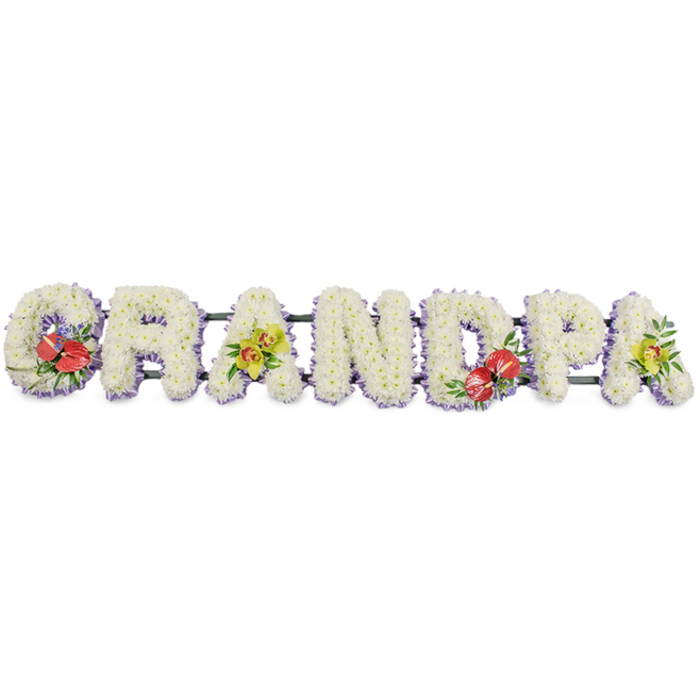 A dignified GRANDPA funeral tribute runs horizontally across the frame, each letter standing tall and clear as if ready to be placed beside a coffin at an Epping service. The letters are constructed in a substantial, block style and completely covered in immaculate white chrysanthemums, the small blooms nestled so tightly together that not a stem is visible. This creates a plush, almost quilted effect, with the rounded petals catching and diffusing the light to convey softness and serenity. At the base of each letter, a band of pastel lavender ribbon forms a discreet border, lending a gentle lilac hue that outlines the shapes and adds a thoughtful finishing touch. The letters are linked by sturdy, dark green bars that sit just beneath the flowers, providing the necessary support without distracting from the design. Colour and character are introduced with carefully positioned sprays of accent flowers: on the G to the left and the D near the centre-right, deep red anthuriums take pride of place, their shiny, heart-shaped bracts and prominent yellow spadices rising from dark, glossy foliage and perhaps a whisper of purple filler blooms. On the first A and the final A, clusters of yellow-green orchids rest on the white cushion of chrysanthemums, their graceful petals and curious, speckled throats adding sophistication and a contemporary feel. A scattering of fresh greenery threads through these sprays, giving them a natural, garden-inspired flow. This type of personalised floral lettering, often ordered from a trusted Epping florist, becomes a touching way to pay tribute to a grandfather's life, offering a clear, bold message of love amid the quiet surroundings of a churchyard or crematorium chapel.